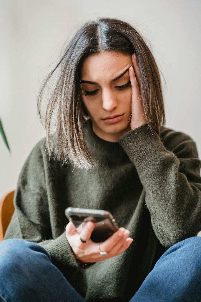 pexels-photo-6383268-6383268 Unhappy female in casual wear leaning on hand and surfing internet on cellphone while sitting in light room near wall at home